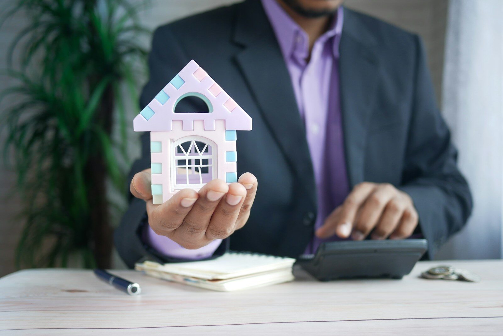 man holding model house at desk with calculator